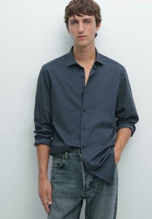Dark blue button-up shirt with a soft texture, standard collar, and rolled cuffs, paired with light grey denim jeans.