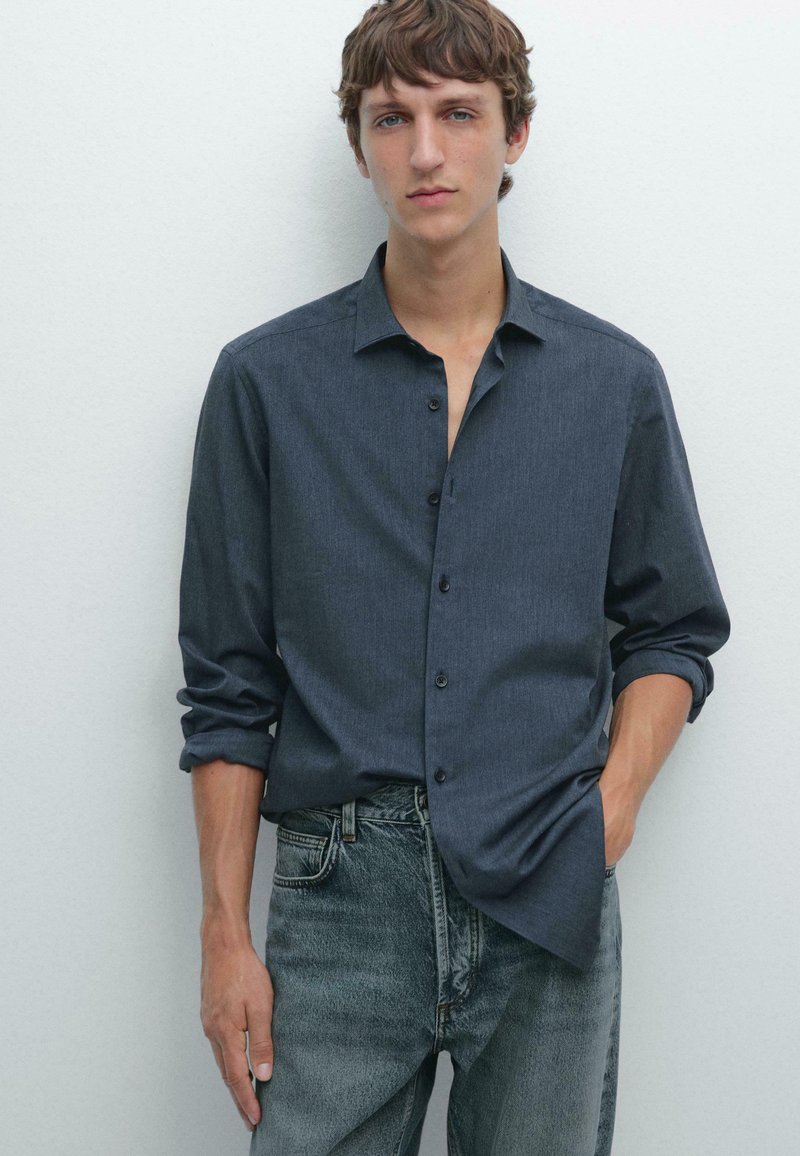 Dark blue button-up shirt with a soft texture, standard collar, and rolled cuffs, paired with light grey denim jeans.