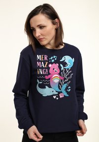 Felpa navy con una stampa colorata e cartoon di un orso rosa e delfini, con la scritta "MERMAZING!" e vari motivi acquatici.