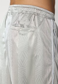 Calções atléticos prateados com um padrão geométrico discreto, faixa elástica na cintura, um único bolso traseiro e detalhes brancos nas laterais.
