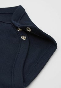 Námornícky modrá bavlněná košile se stříbrnými patentkami; má hladkou texturu a žebrované okraje na límci a rukávech.