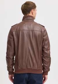 Veste en cuir marron avec des poignets et un col côtelés, dotée d'épaules épaulettes et d'une texture lisse, vue de dos.