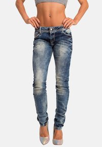 Jeans skinny in denim blu sbiadito, con dettagli strappati e leggere sfumature. Abbinati a un top grigio cropped e tacchi metallici.