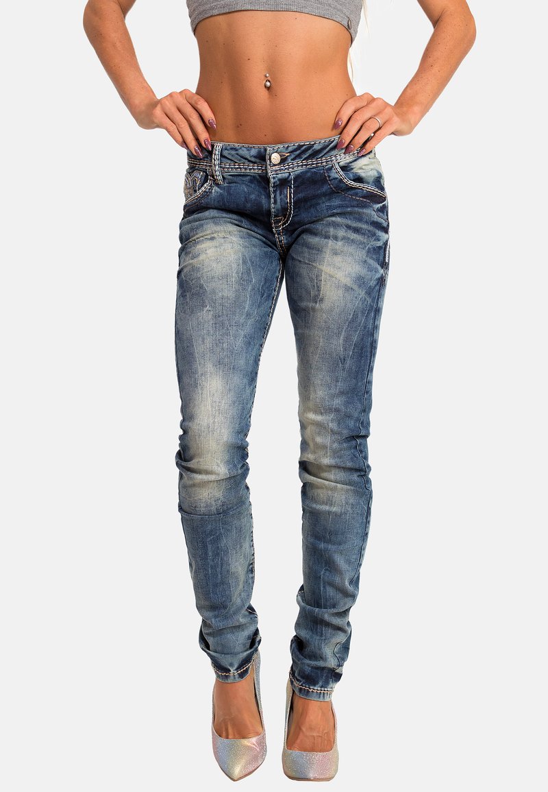 Jeans skinny in denim blu sbiadito, con dettagli strappati e leggere sfumature. Abbinati a un top grigio cropped e tacchi metallici.