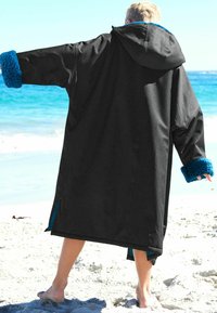 Svart ytterplagg med huva, med ljusblå fleeceärmar. Materialet är slätt och designen är oversized med sidofickor.