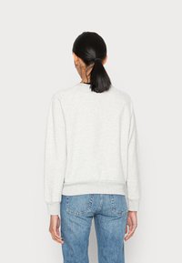 Sweatshirt gris clair avec un col rond côtelé et des poignets, présentant un design simple. Associé à un jean en denim à délavage moyen.