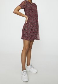 Robe à motif floral avec des manches courtes et un col rond, présentant un motif rouge et noir. Assortie à des baskets blanches épaisses.