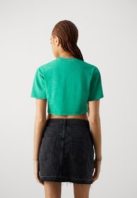 Camiseta verde corta de manga corta, hecha de suave algodón. Combinada con una falda de mezclilla negra con bolsillos traseros y dobladillo deshilachado.
