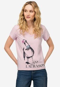 Camiseta de algodón rosa con cuello en V que presenta un gráfico de un pingüino en negro y rosa, con el texto "LAURASON" debajo, combinada con unos jeans azules.