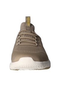 Beige Sportschuh mit strukturiertem Strick-Obermaterial und weißer Sohle. Besitzt ein gelbes Etikett an der Ferse und elastische Schnürsenkel für einen sicheren Sitz.