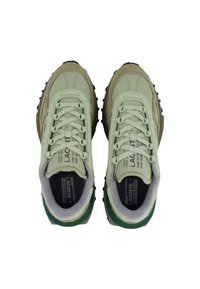 Par de zapatillas Lacoste en verde y beige con suelas texturizadas y plantillas con la marca, vistas desde arriba sobre un fondo blanco.