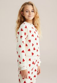 Set de loungewear din fleece crem cu modele de inimioare roșii. Include manșete și talie cu dantelă, textură moale și croială lejeră.