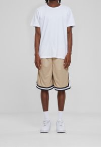 T-shirt blanc à manches courtes associé à un short en mesh beige avec des rayures noires et blanches le long de l'ourlet, complété par des baskets blanches.