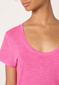 Prilegajo kratkimi rokavi v svetlo roza barvi, z širokim izrezom v obliki črke U in mehko, teksturirano tkanino.