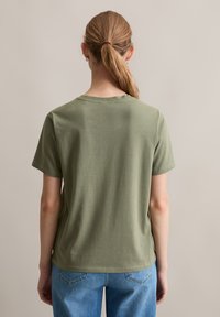 T-shirt olive à manches courtes avec col rond, texture douce et coupe droite. Associé à un jean en denim bleu clair.