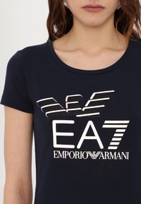 Jūrų laivyno trumpomis rankovėmis marškinėliai su ryškiu daugiakultūriu grafiniu logotipu "EA7 EMPORIO ARMANI", turintys minkštą tekstūrą ir apvalų kaklo dizainą.