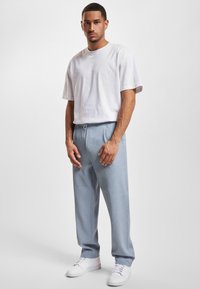 Camiseta blanca de algodón con mangas cortas, combinada con pantalones de rayas finas en azul claro y zapatillas blancas. Ajuste simple y relajado, con detalles mínimos.