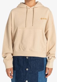 Beige hættetrøje med en frontal lomme, snoretræk og gyldt logo på brystet; har en afslappet pasform og blød tekstur.