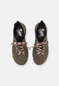 Baskets vert olive en suède texturé, avec des lacets à carreaux contrastés, des zippers sur les côtés et une doublure intérieure noire. Semelle blanche avec des accents de couture.