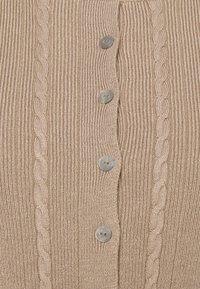Tissu tricoté beige avec côtes verticales et motifs torsadés, comprenant une colonne de quatre boutons ronds beiges.
