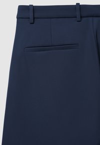 Pantaloni blu navy caratterizzati da una superficie liscia, una vita piatta, passanti per cintura e una tasca posteriore singola. Taglio sartoriale per un look aderente.