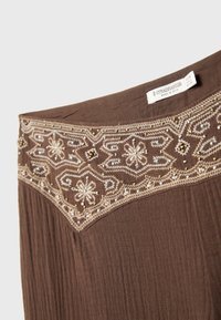 Brun tygkjol med en broderad midja som har blommönster och spridda pärlor i guld och blått. Lappen läser "Stradivarius, tillverkad i Indien."