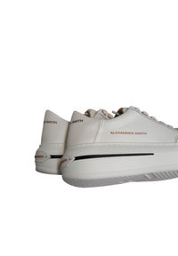 Hvide sneakers med en glat læderoverdel, flade snørebånd og subtilt prægede branding. Har en tyk sål med en sort accentstribe.
