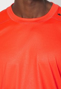 Camiseta deportiva roja con una tela texturizada y transpirable con un patrón de panal y un cuello redondo.