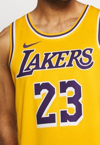 Camiseta de baloncesto amarilla de los Lakers con el número 23 en púrpura y el logo de Nike, llevada por una persona, recortada a la altura del pecho y el cuello.