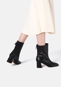 Bottines en cuir noir avec bout carré, talon bloc de hauteur moyenne et fermetures éclair latérales. Texture lisse avec un design élégant.