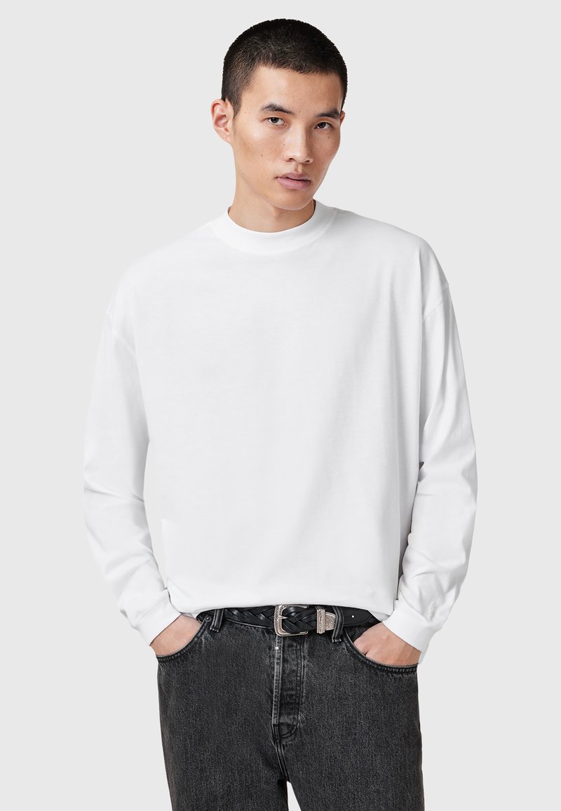 Weißes Langarmshirt mit Rundhalsausschnitt aus Baumwolle, kombiniert mit dunkelgrauen Jeans. Das Shirt hat eine lockere Passform und einen gerippten Ausschnitt.