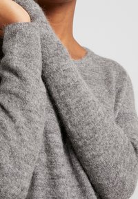 Grå stickad tröja med en mjuk, texturerad yta och långa ärmar, med en rund halsringning och en något avslappnad passform.