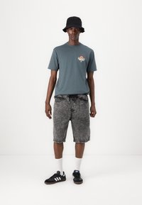 Gray T-shirt with a graphic print, black denim shorts, black bucket hat, black sneakers with white stripes, and white socks.