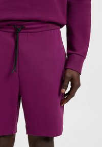 Purple sweat shorts featuring an elastic waistband with a black drawstring. Made from soft fabric with a smooth texture and side seams.