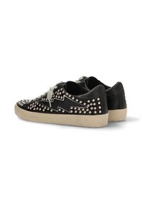 Zapatillas negras con tachuelas metálicas, que presentan un diseño en zigzag en el lateral, cordones grises y una suela de goma crema.