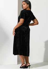 Czarna aksamitna sukienka midi z krótkimi rękawami, o gładkiej fakturze i lekko rozkloszowanym kroju. W połączeniu z czarnymi szpilkami.