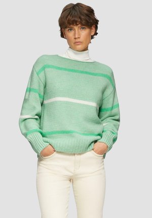 Grüner und weiß gestreifter Pullover aus weichem Strickstoff mit gerippten Bündchen und Saum, getragen über einem weißen Rollkragenpullover und kombiniert mit hellen Hosen.