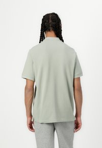 Light green polo shirt with a relaxed fit, short sleeves, and side slits. Cotton fabric with a smooth texture, shown from the back.