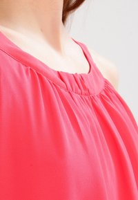 Rosa ärmellose Bluse mit einem gerafften Ausschnitt und weichem, fließendem Stoff mit glatter Textur. Das Design umfasst zarte Falten.