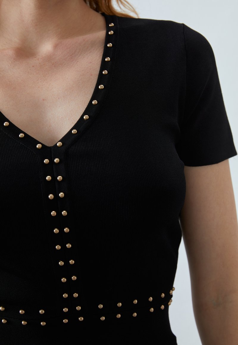 Czarny dopasowany top z krótkimi rękawami, dekoltem w kształcie litery V i złotymi ćwiekami wzdłuż dekoltu oraz dołu, tworzącymi teksturalny akcent. Materiał prążkowany.