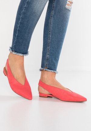 Kobieta nosząca jasnoróżowe baleriny typu slingback zestawione z niebieskimi, obcisłymi dżinsami z postrzępionym brzegiem i przetarciem na kolanie.