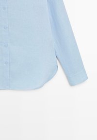 Lichtblauw overhemd met lange mouwen, knoopsluiting, afgeronde zoom en manchetten met één knoop, getoond van borst tot mouw op een witte achtergrond.