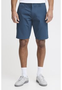 Blue cotton shorts with a flat front, two side pockets, and a button closure. Worn with light gray sneakers and white socks.