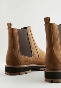 Botas Chelsea marrones de ante sintético con paneles laterales elásticos, suelas de goma resistentes y detalles de costura en contraste.