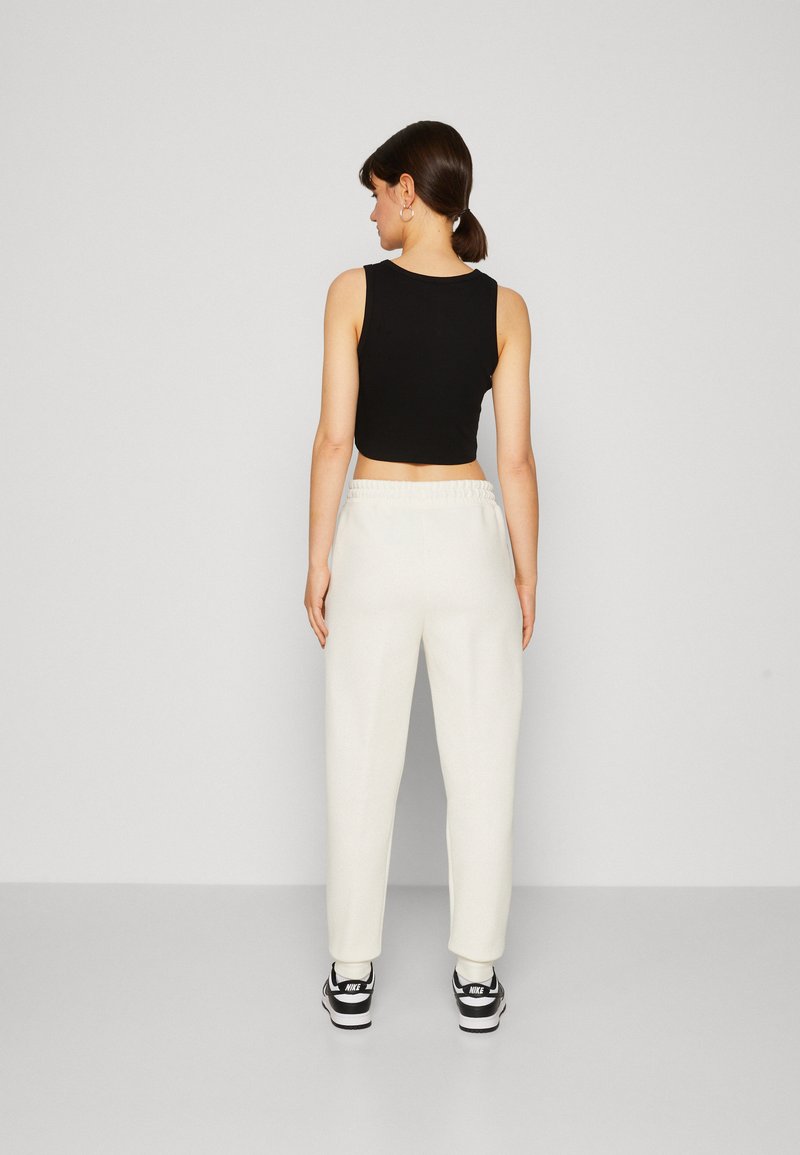 Cropped top nero, pantaloni bianchi a vita elastica con vestibilità rilassata, indossati con sneakers bianche e nere. Tessuto liscio, design semplice.