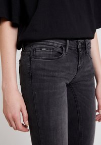 Vaqueros de mezclilla negra con un corte slim, que presentan un diseño clásico de cinco bolsillos, costuras sutiles y una etiqueta en el bolsillo trasero.