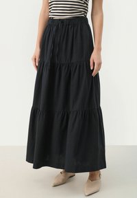 Svart tiered maxikjol gjord av lättviktigt tyg med elastiskt midjeband. Kompletteras av beige spetsiga ballerinas.