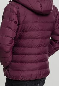 Ciemnofioletowa kurtka puchowa z poziomym pikowaniem, z przymocowanym kapturem i gładką fakturą. Posiada regulowany troczek przy kapturze.