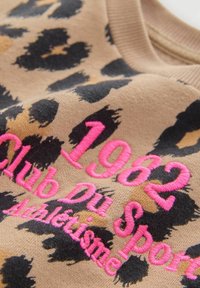 Tissu à motif léopard dans des tons de beige et noir, avec un texte brodé en rose : "1962 Club Du Sport Athlétisme." Texture douce.