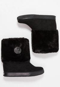 Botas de tobillo de ante negro con cuña, con un grueso puño de piel sintética y una insignia metálica redonda en el lado exterior.